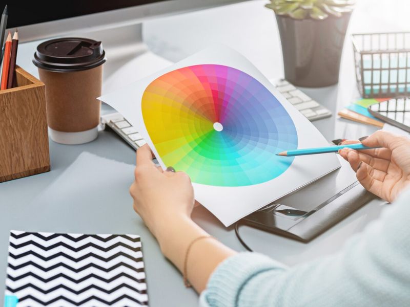Círculo Cromático: O Guia para Combinações de Cores Perfeitas 1 circulo-cromatico, imagem mostra pessoa apontando um lapis azul para a imagem de um circulo cromatico