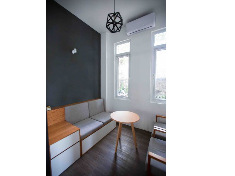 Como Decorar Ambientes Pequenos - 11 Dicas e Layout 1 imagem mostra um ambiente pequeno com uma parede pintada de preto, um sofa, uma mesa de centro redonda e duas poltronas. O ambiente possui ainda duas janelas retangulares e uma luminaria pendente preta
