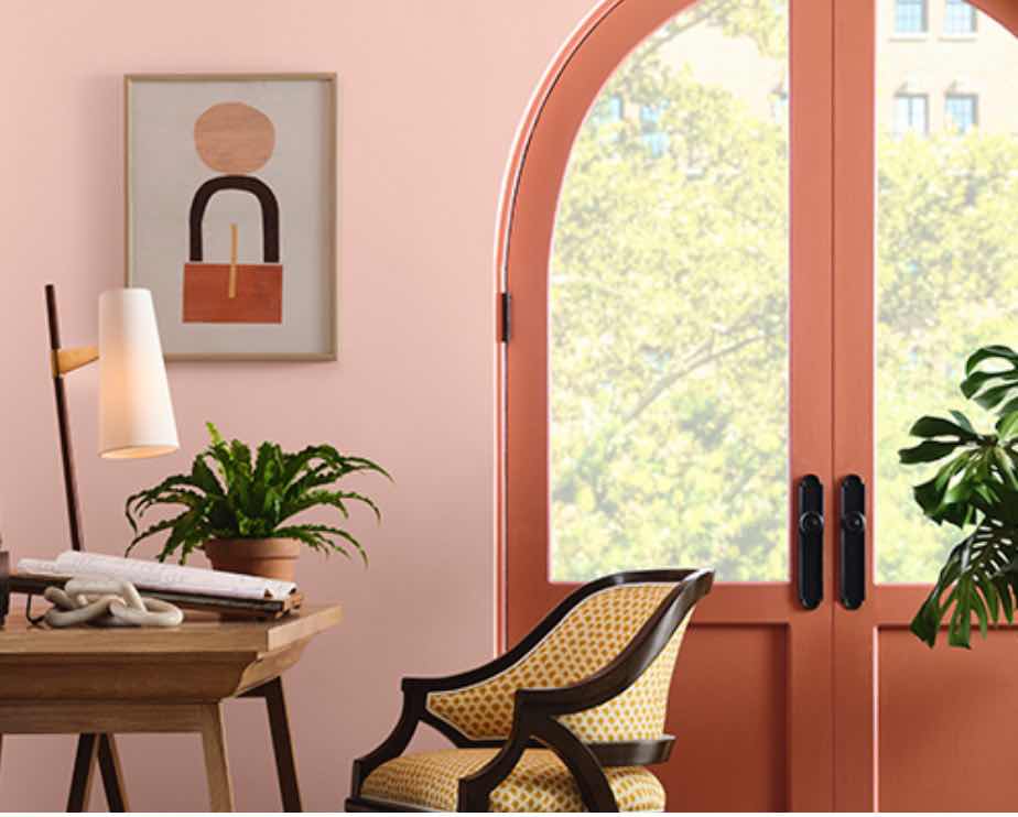 As Cores De Tinta Do Ano 2025 4 cores de tinta do ano 2025, imagem mostra parede em tom rosado, uma porta de vidro na cor rosa mais escura, mesa com alguns objetos de decoração e cadeira