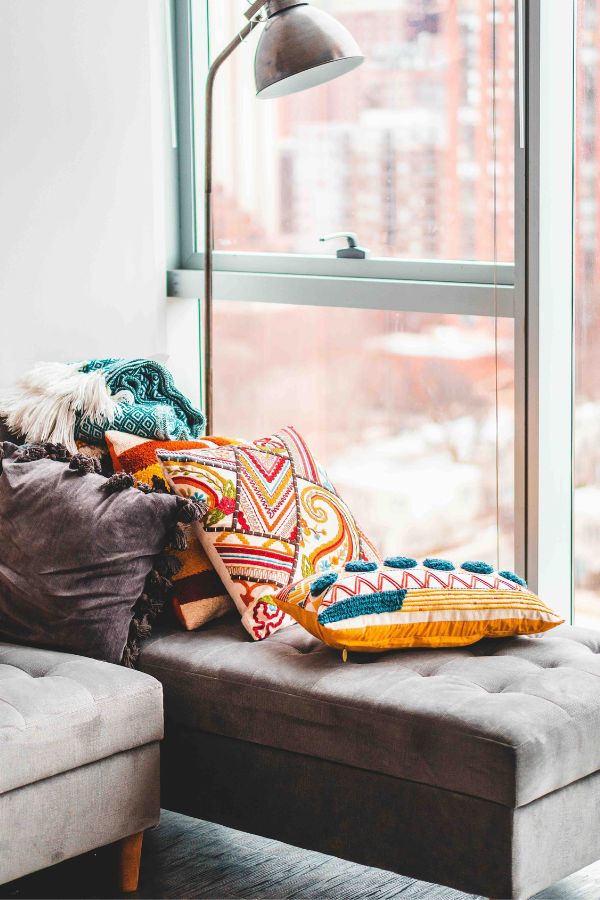 Como Misturar Padrões De Tecidos Na Decoração 2 Como Misturar Padrões De Tecidos Na Decoração, imagem mostra um banco revestido em tecido liso e bege, com várias almofadas estampadas e coloridas jogadas por cima dele