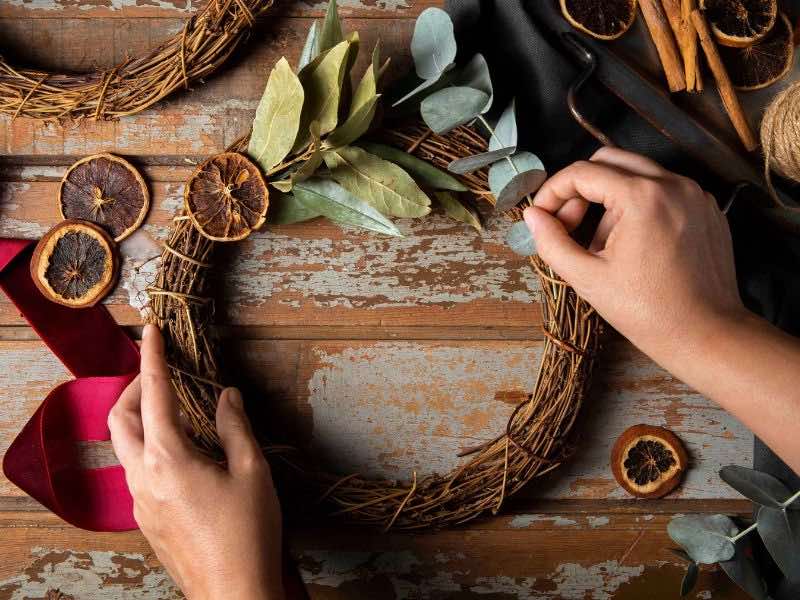 Decorando Para Natal: Um Convite à Magia da Decoração ✨️ 3 decorando-para-natal, imagem mostra pessoa fazendo uma guirlanda de galhos secos com enfeites de frutas e folhas